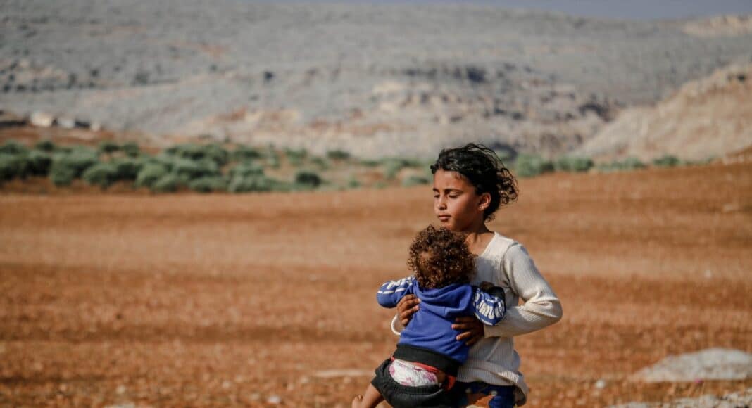 ethnic girl with baby in arms walking on rural field