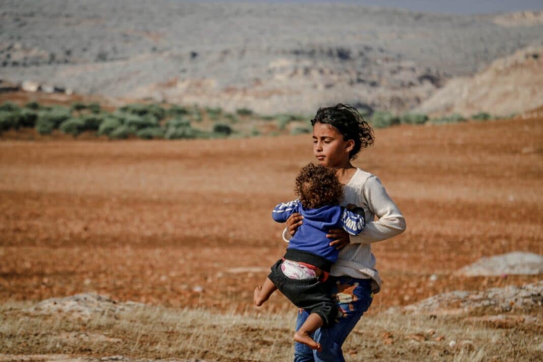ethnic girl with baby in arms walking on rural field
