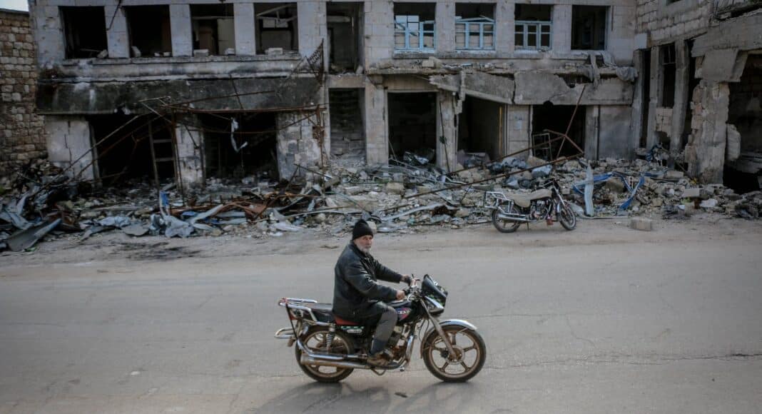man riding motorbike along destroyed building