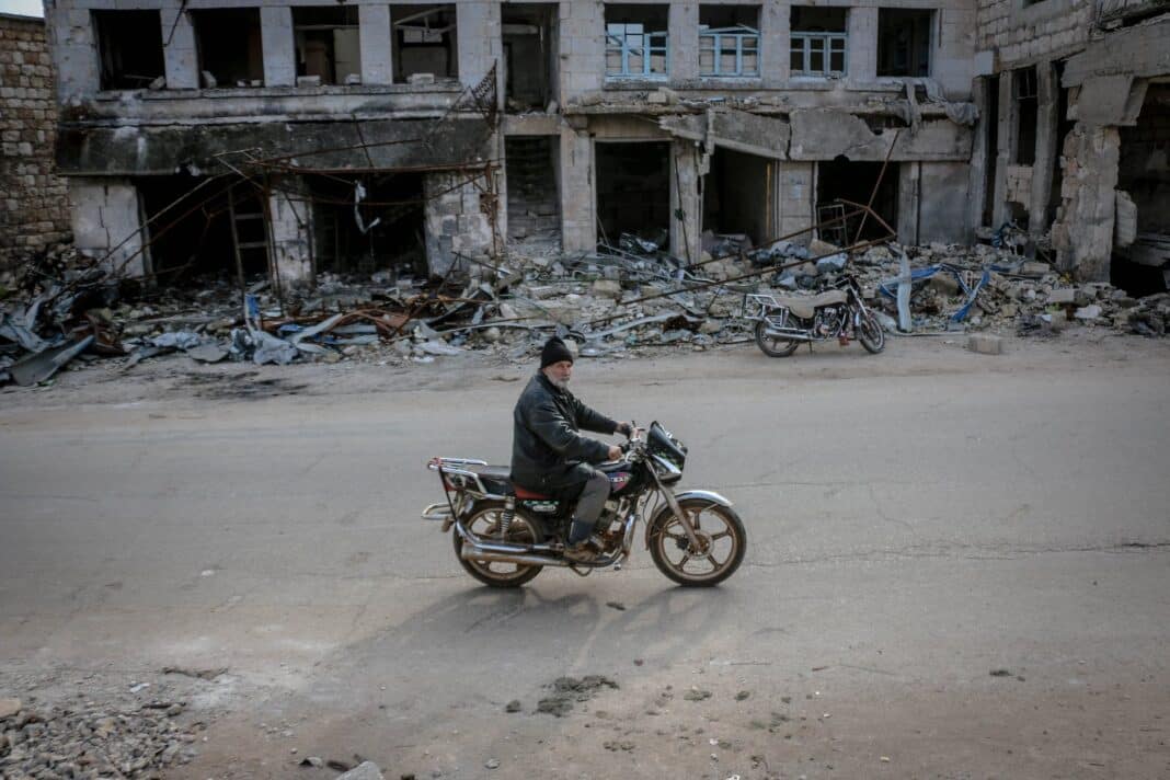 man riding motorbike along destroyed building