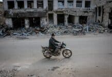 man riding motorbike along destroyed building
