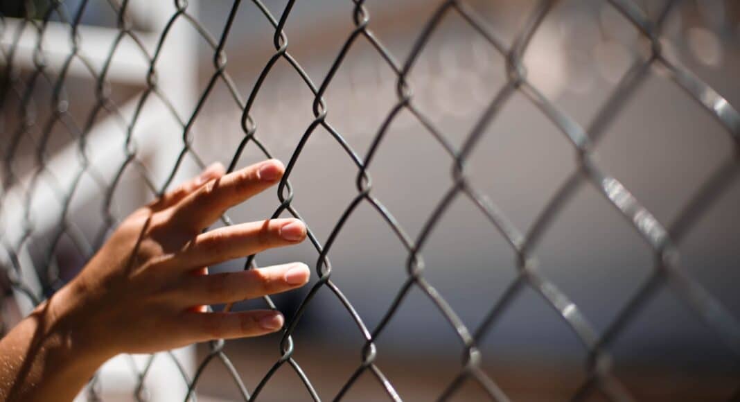 hand of crop person touching grid fence