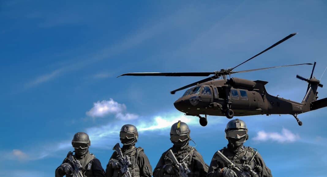 four soldiers carrying rifles near helicopter under blue sky
