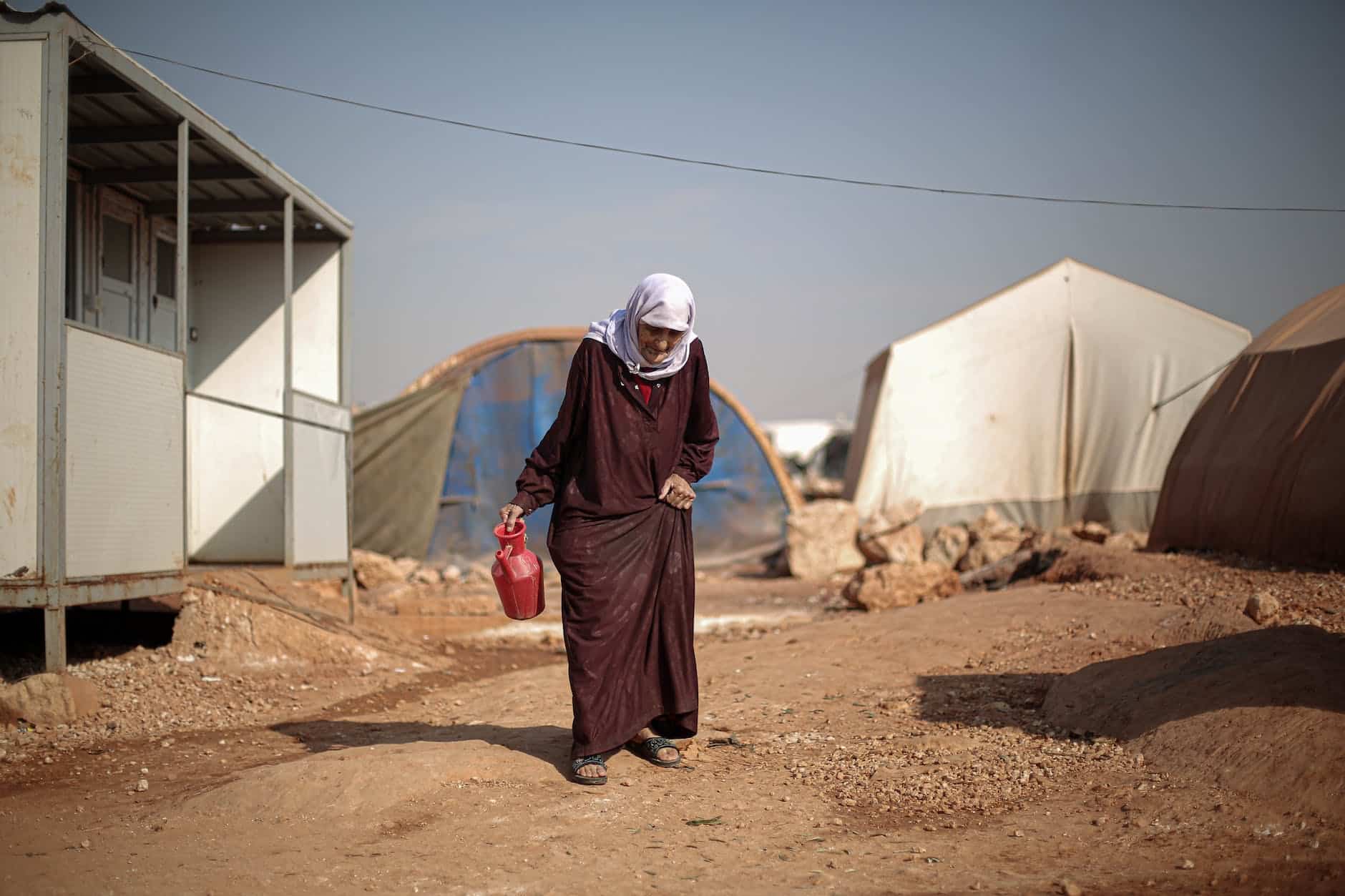 elderly woman walking through campsite in warzone in syria