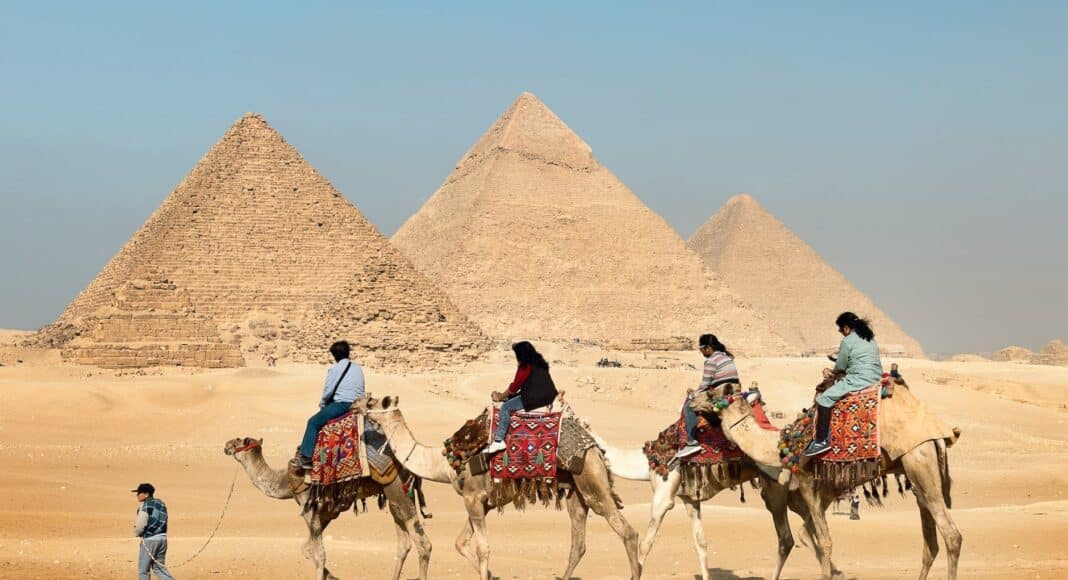four people riding on camels across the pyramids