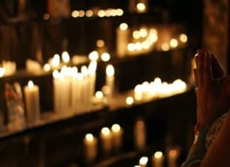 close up photograph of person praying in front lined candles
