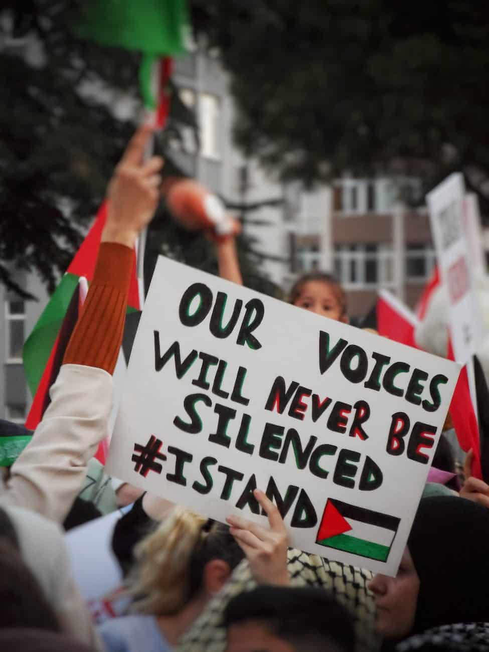 Impuissants face aux combattants, ils bombardent les civils ! a sign that reads our voices will never be silenced israel