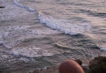woman in brown hijab sitting on the cliff near the ocean