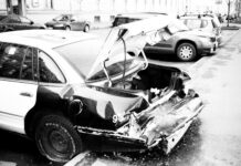grayscale photo of wrecked car parked outside