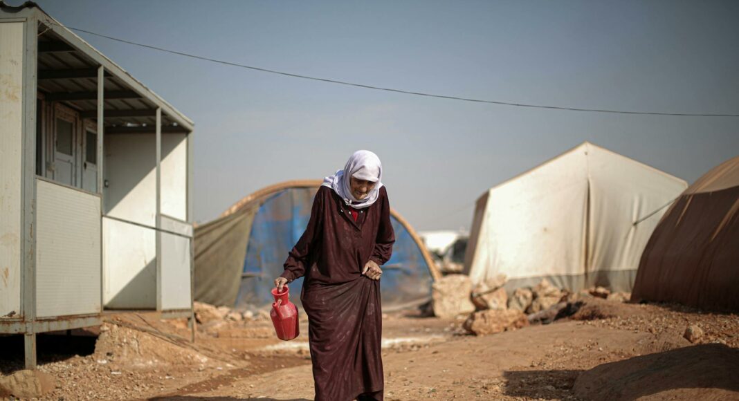 elderly woman walking through campsite in warzone in syria