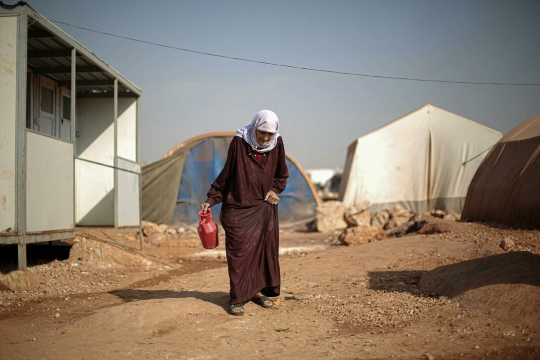 elderly woman walking through campsite in warzone in syria