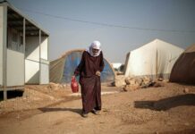elderly woman walking through campsite in warzone in syria