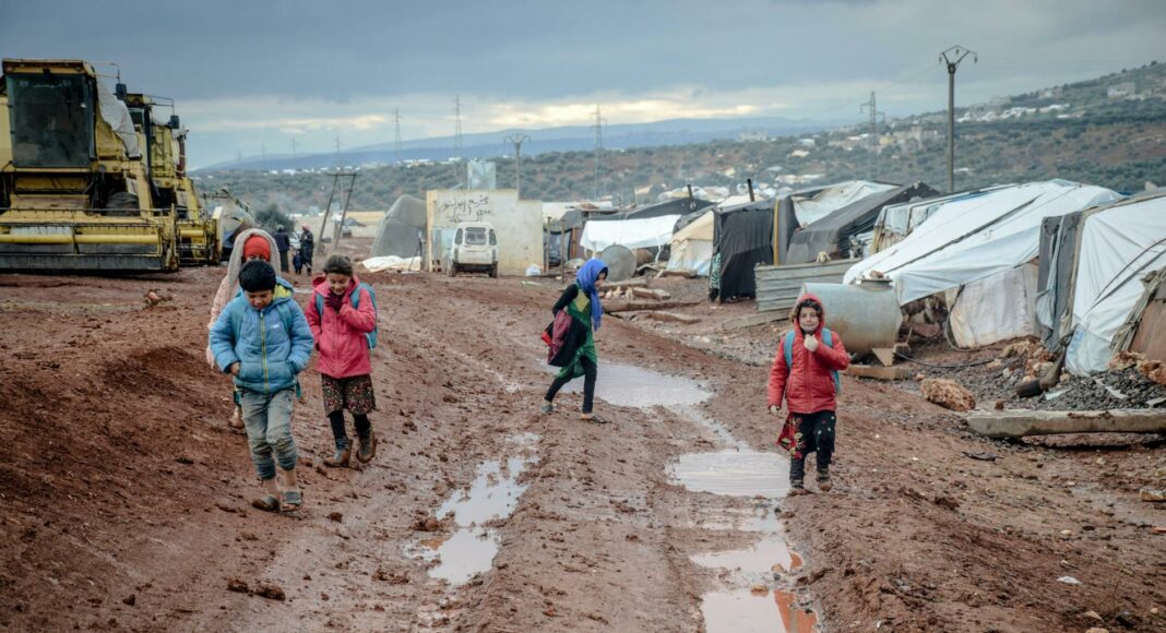 poor children walking on muddy ground in settlement with tents