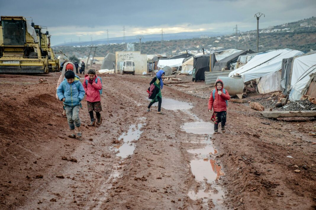 poor children walking on muddy ground in settlement with tents