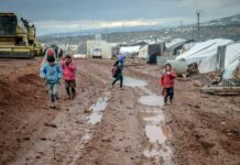 poor children walking on muddy ground in settlement with tents