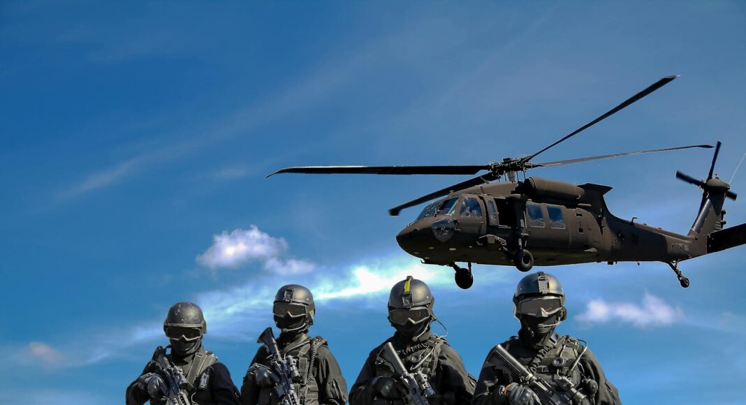 four soldiers carrying rifles near helicopter under blue sky