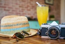 gray and black dslr camera beside sun hat and sunglasses