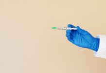 crop nurse with syringe on beige background