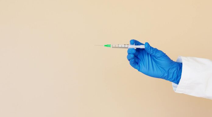 crop nurse with syringe on beige background