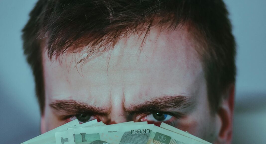 serious young male covering face with banknotes