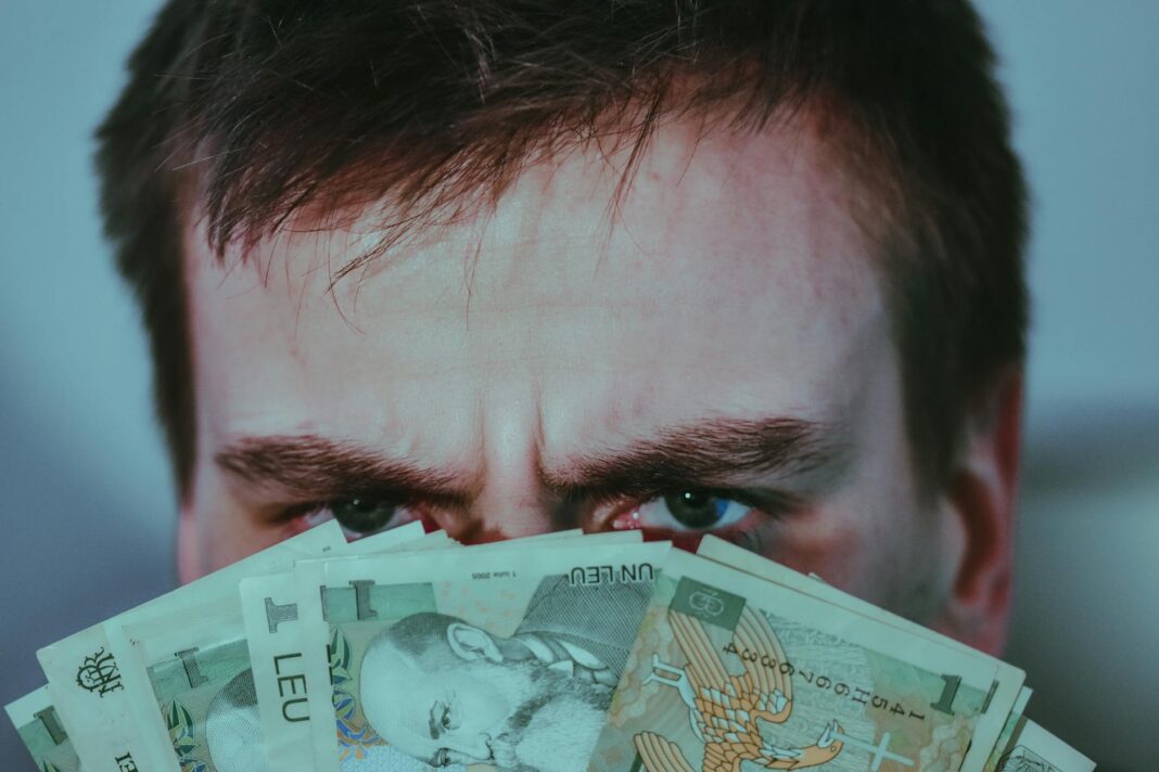 serious young male covering face with banknotes