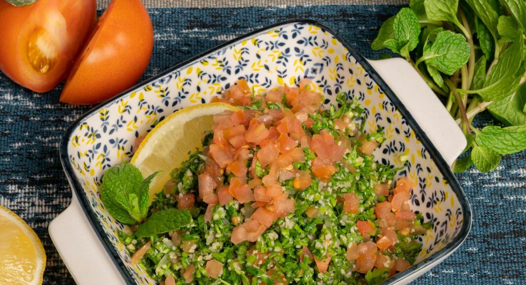 a bowl of salad with tomatoes parsley and lemon