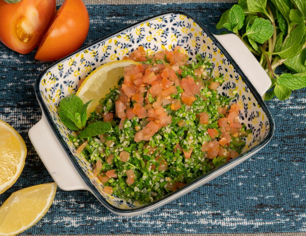 a bowl of salad with tomatoes parsley and lemon