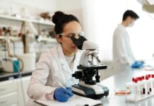 female scientist in white lab coat using a microscope