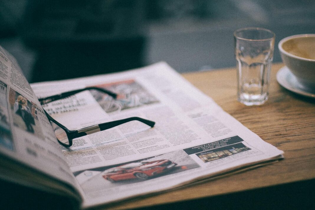 eyeglasses on magazine near glass on cafe table