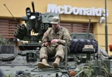 man in brown camouflage sitting on top of tank