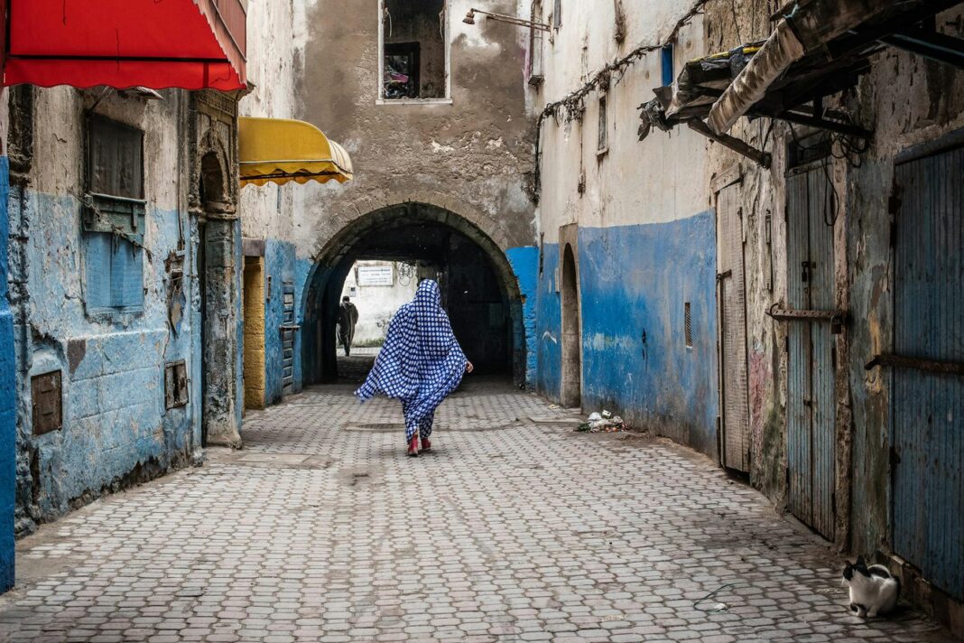 back of a woman wearing a polka dot jilbab walking along a paved alley