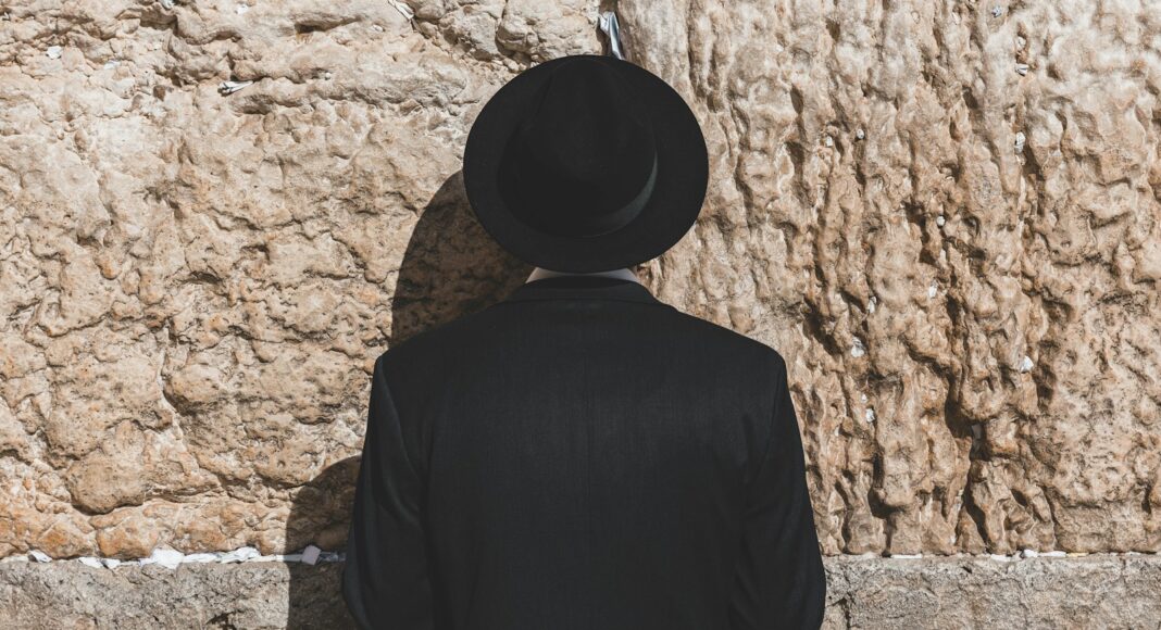 a man wearing a black hat standing in front of a stone wall