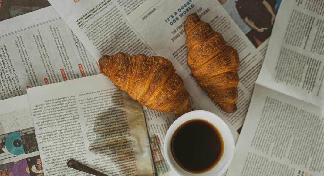white ceramic mug with coffee beside brown bread on white paper