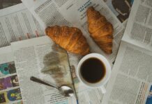 white ceramic mug with coffee beside brown bread on white paper