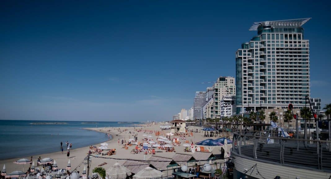 a crowded beach with umbrellas and buildings in the background