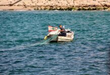 man wearing black and gray striped shirt sitting on white boat on blue body of water during daytime