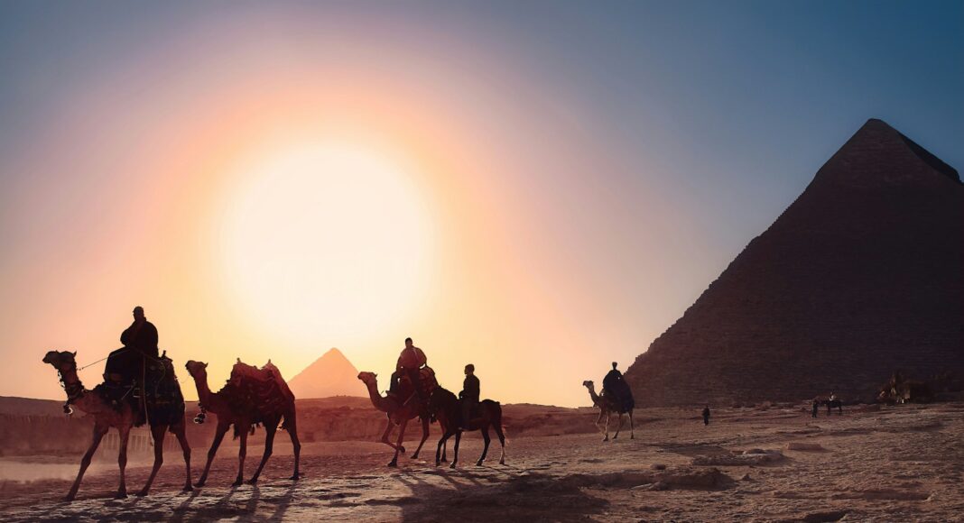 five persons riding camels walking on sand beside Pyramid of Egypt