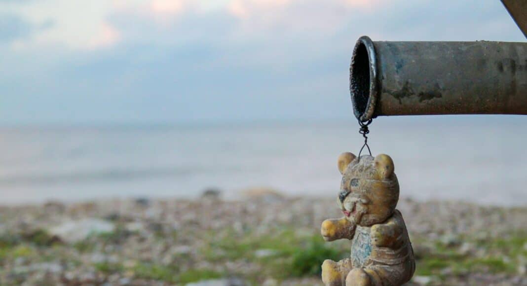 a teddy bear hanging from a pipe near a body of water