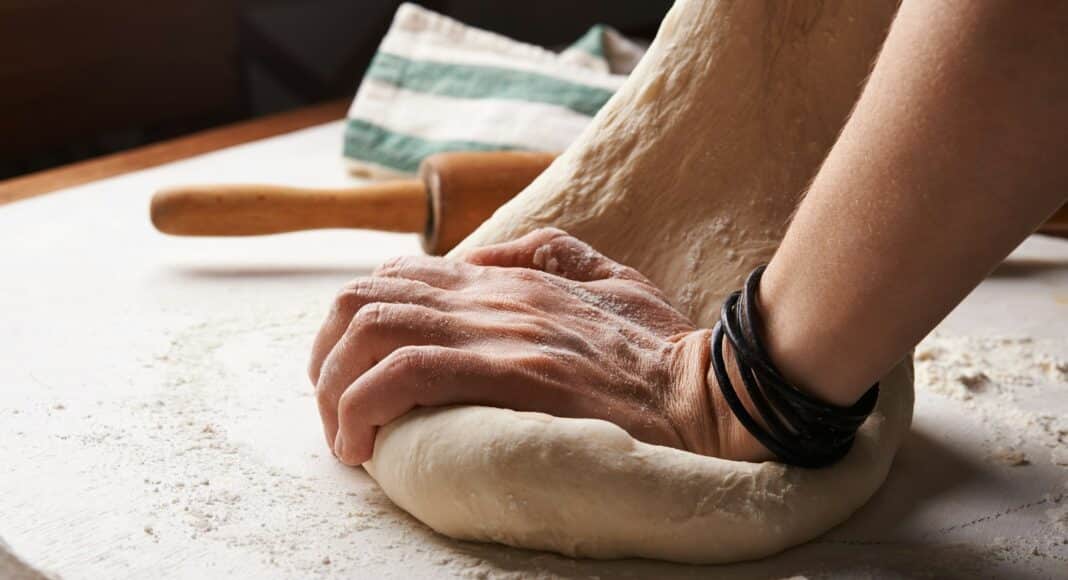 person making dough beside brown wooden rolling pin