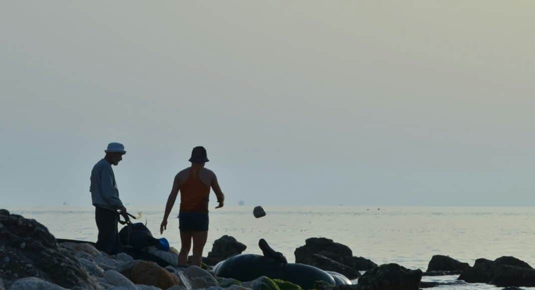 A couple of men standing on top of a rocky beach