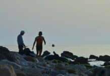A couple of men standing on top of a rocky beach