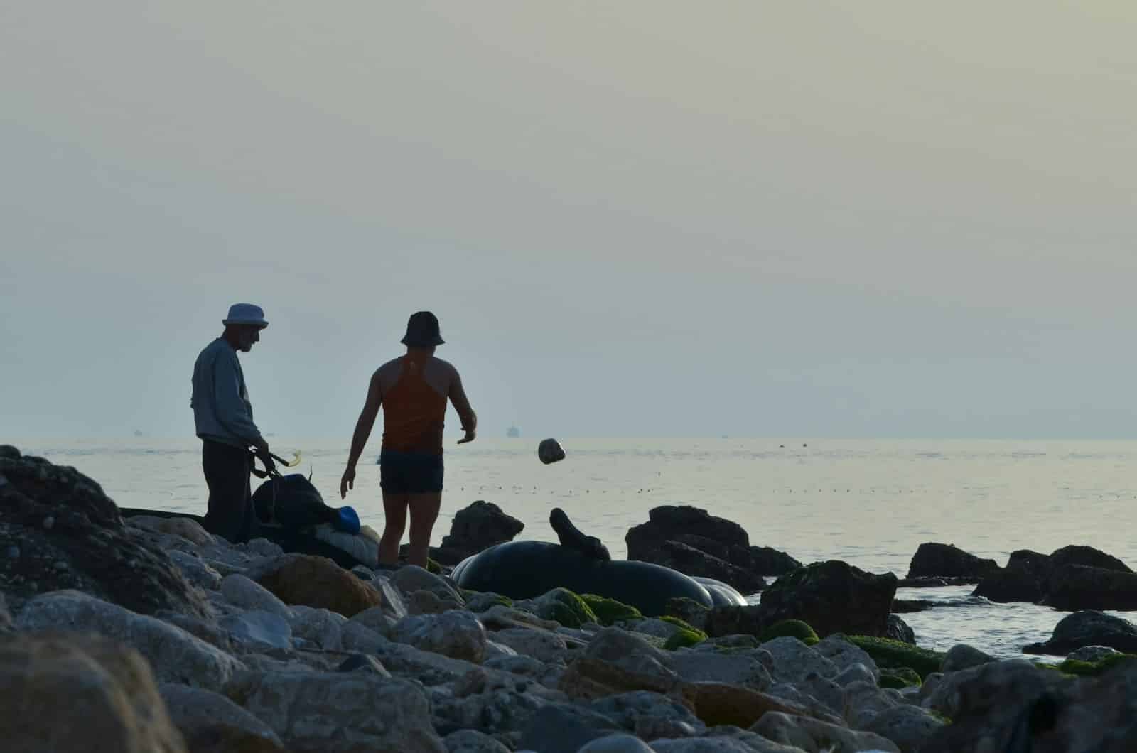 A couple of men standing on top of a rocky beach
