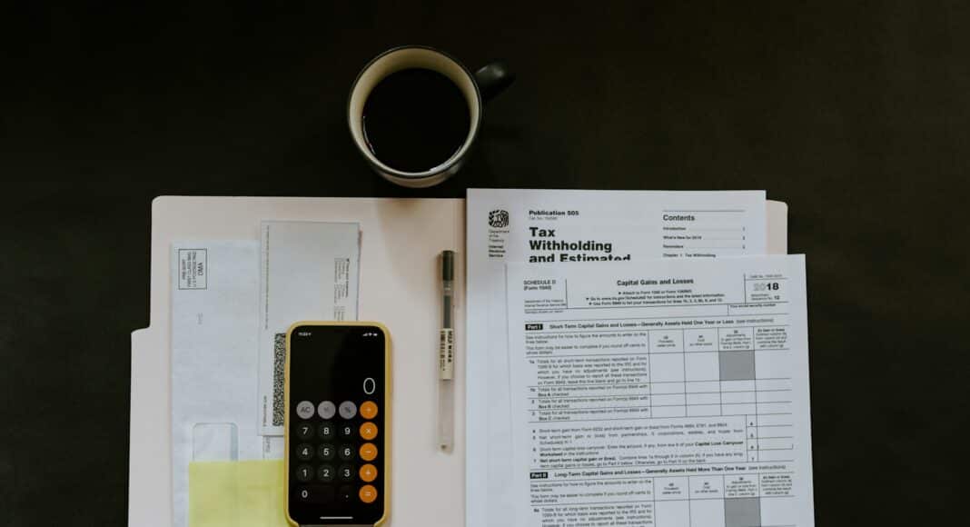 black Android smartphone near ballpoint pen, tax withholding certificate on top of white folder