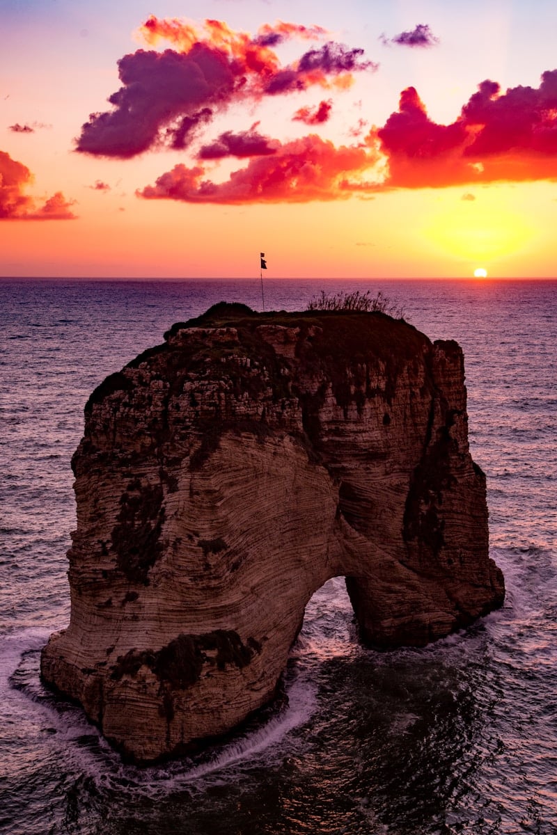 flag on top of rock formation in the middle of sea