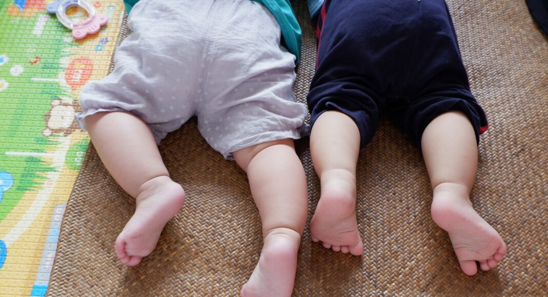 baby in white shirt and black pants lying on brown carpet