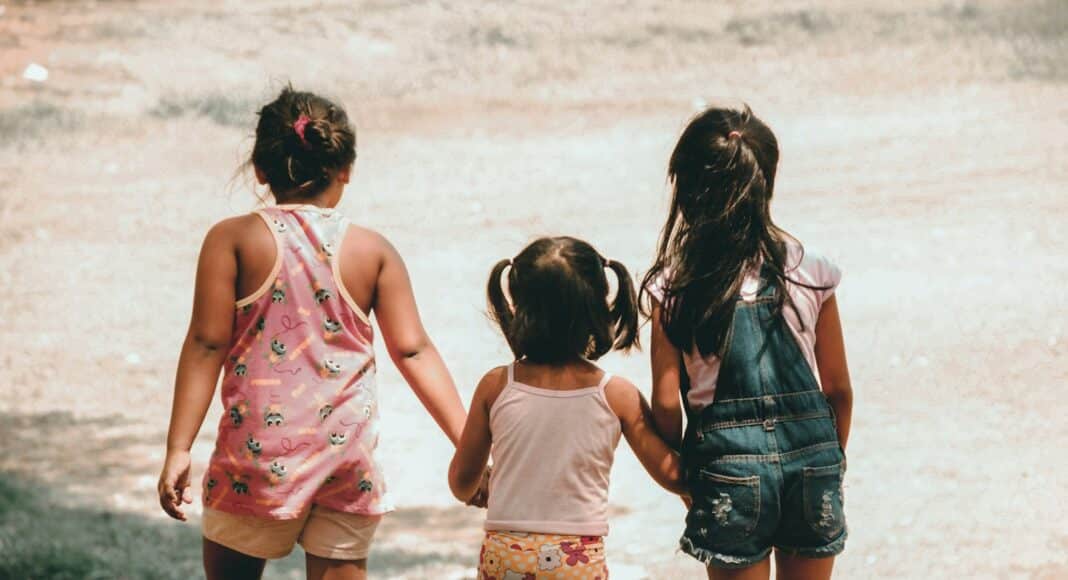 three girls holding each other hand walking towards brown soil