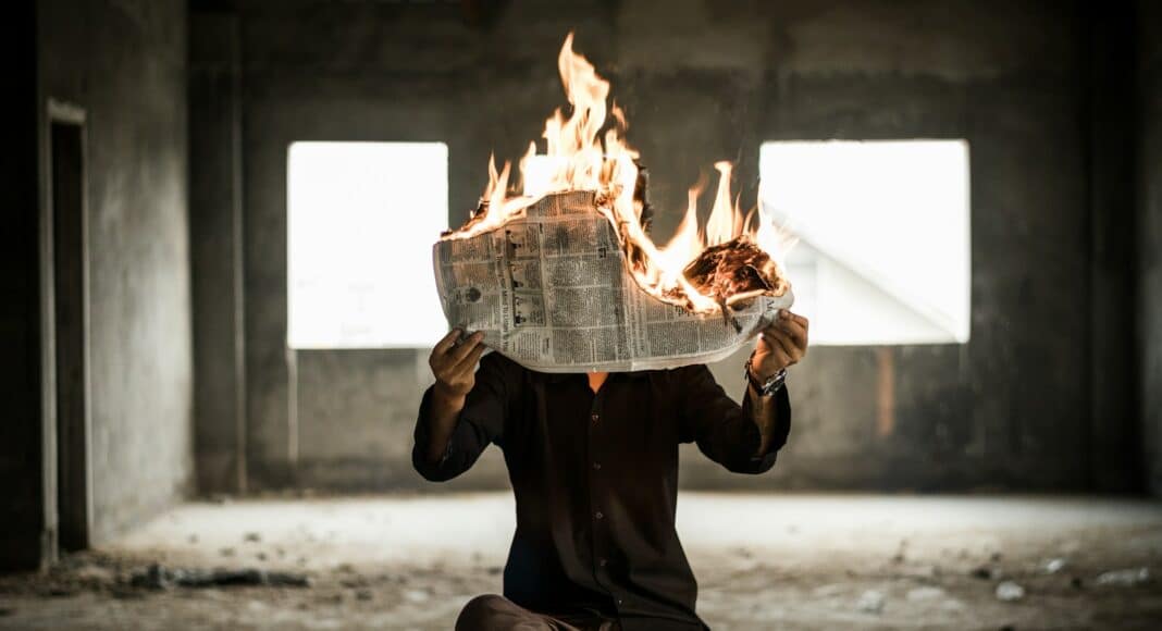 man sitting on chair holding newspaper on fire