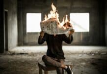 man sitting on chair holding newspaper on fire