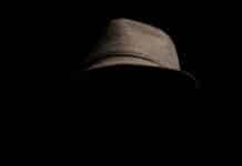 person wearing gray plaid notched lapel suit jacket and gray hat hiding face