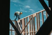man in yellow shirt and blue denim jeans jumping on brown wooden railings under blue and